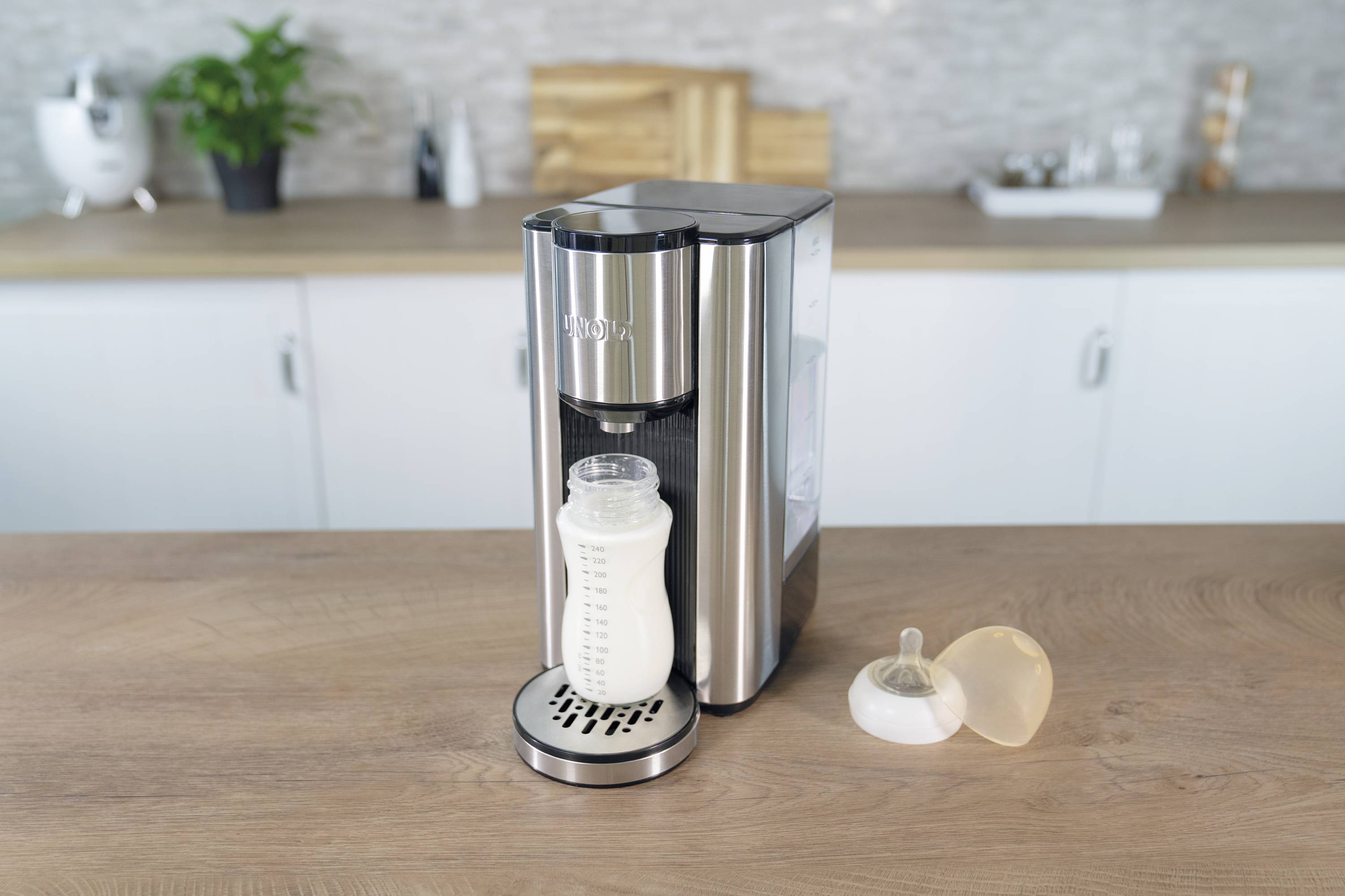 Milchflaschen-Wärmer auf einer Küchenarbeitsplatte, gefüllt mit einer Milchflasche. Neben der Flasche liegt ein Sauger.