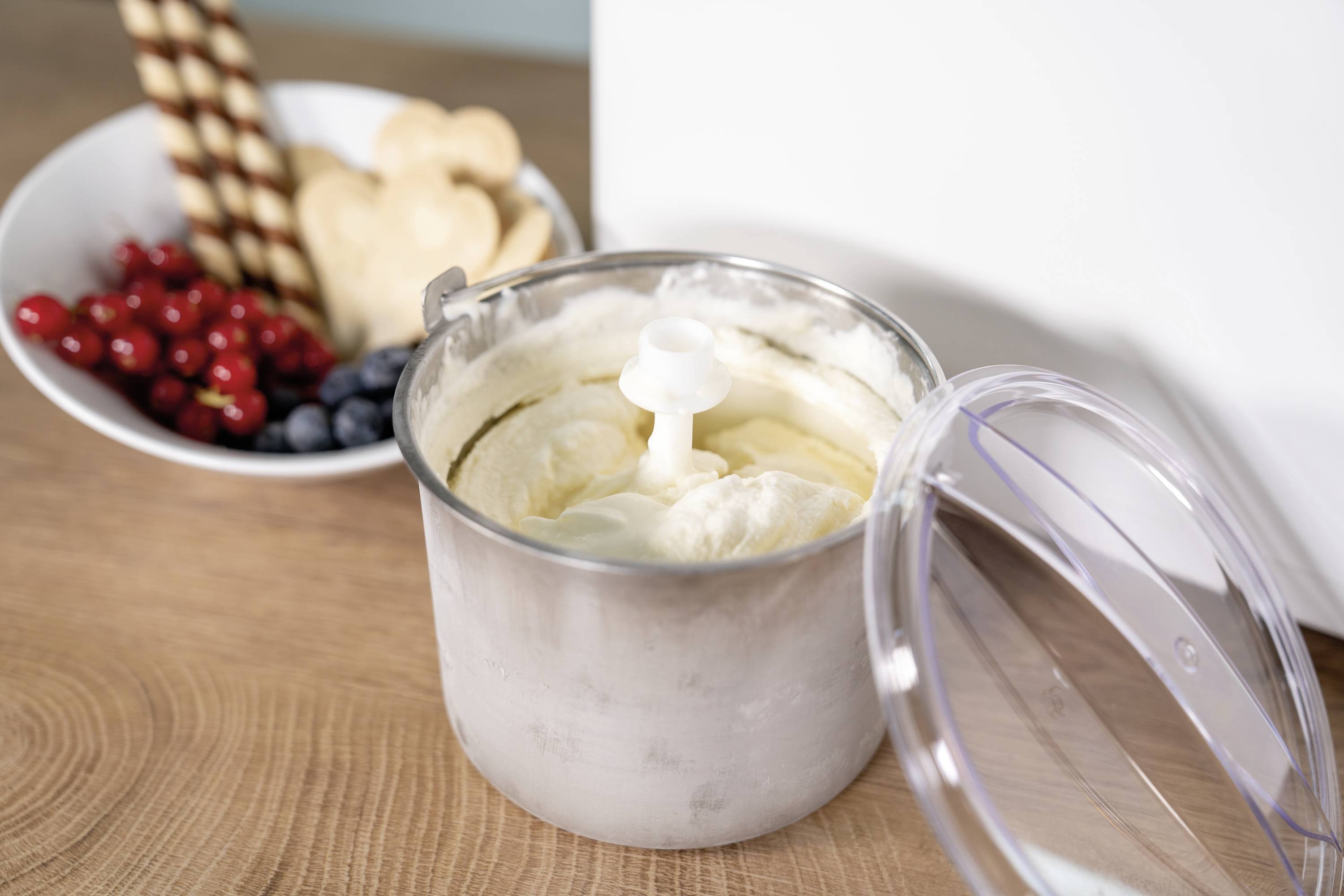 Offener Eisbehälter mit frisch gemachtem Vanilleeis. Im Hintergrund eine Schüssel mit Keksen, Johannisbeeren und Blaubeeren.