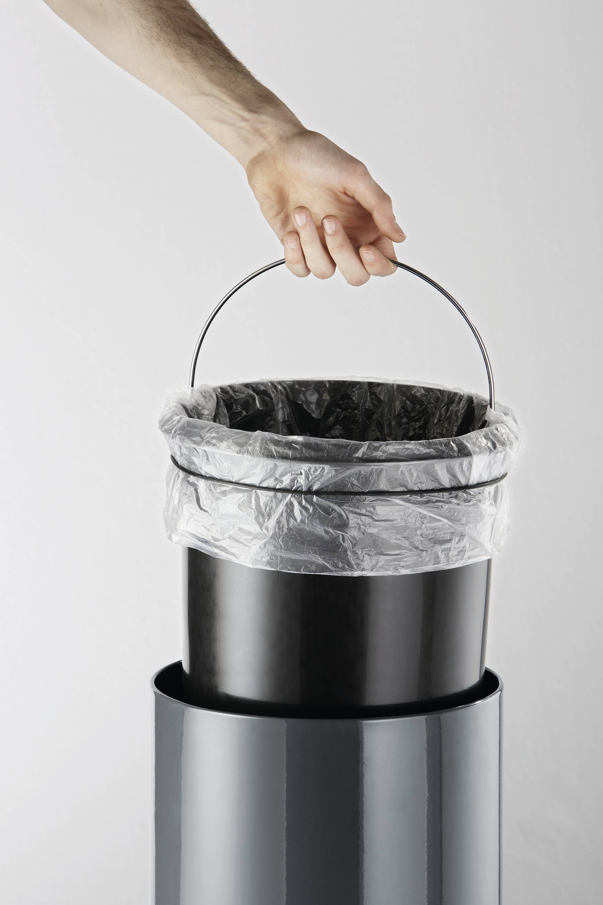 Eine Hand hebt einen Mülleimer aus einem größeren Behälter. Der Mülleimer ist mit einem transparenten Plastikbeutel ausgekleidet.