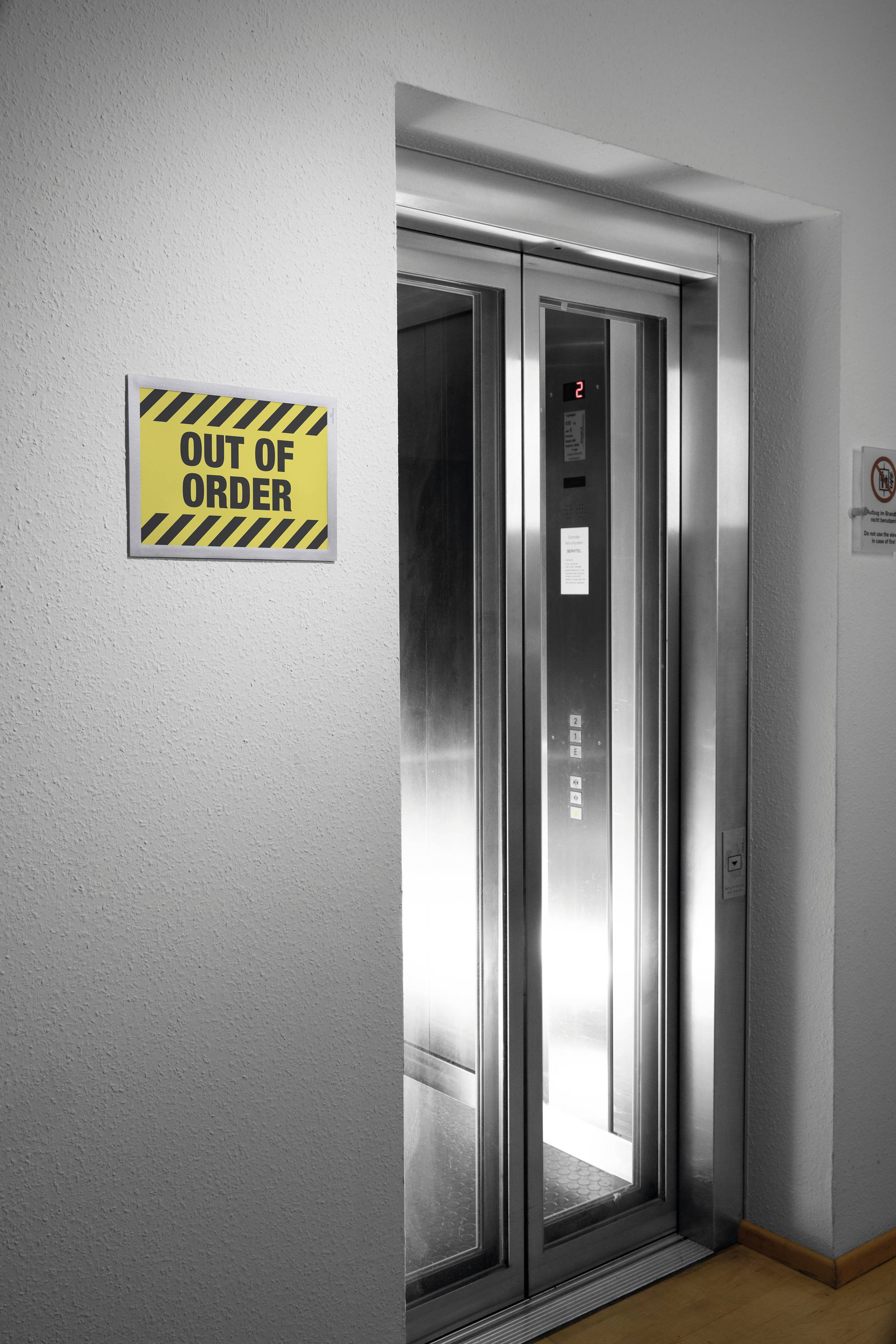 Ein Aufzug mit geöffneten Türen zeigt ein 'Out of Order'-Schild an der Wand. Der Aufzug steht still und ist derzeit außer Betrieb.