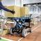Ein Arbeiter schiebt einen hydraulischen Hubwagen mit großen Kartons in einem Lager. Im Hintergrund sind Regale und weitere Kartons zu sehen.