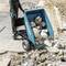 Eine Person bedient eine elektrische Schubkarre mit großen Steinen auf einer Baustelle. Die Konstruktion im Hintergrund deutet auf Bauarbeiten hin.
