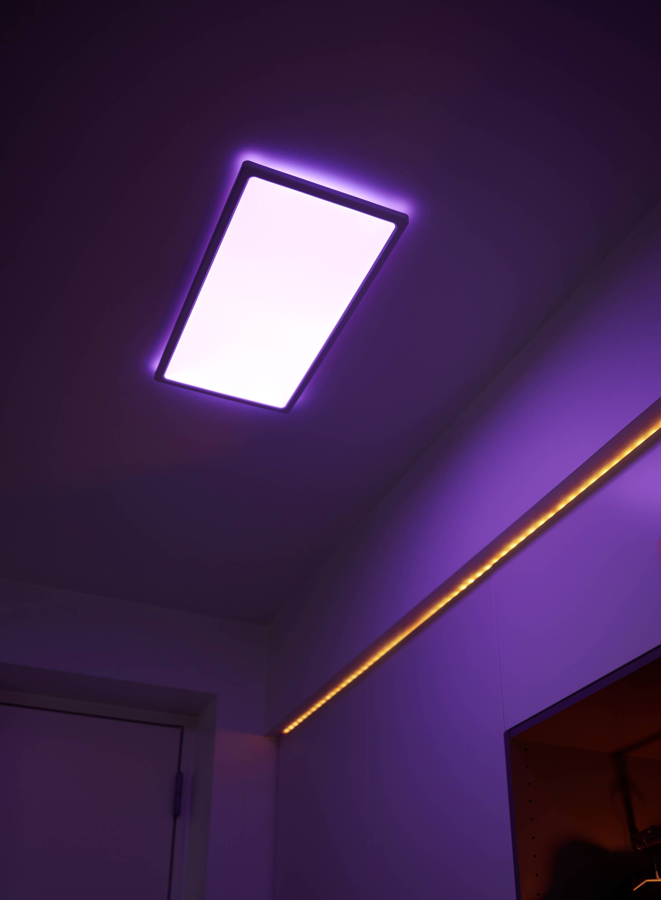 Eine rechteckige Deckenleuchte strahlt violettes Licht aus. Ein daneben verlaufender Lichtstreifen leuchtet in orange.