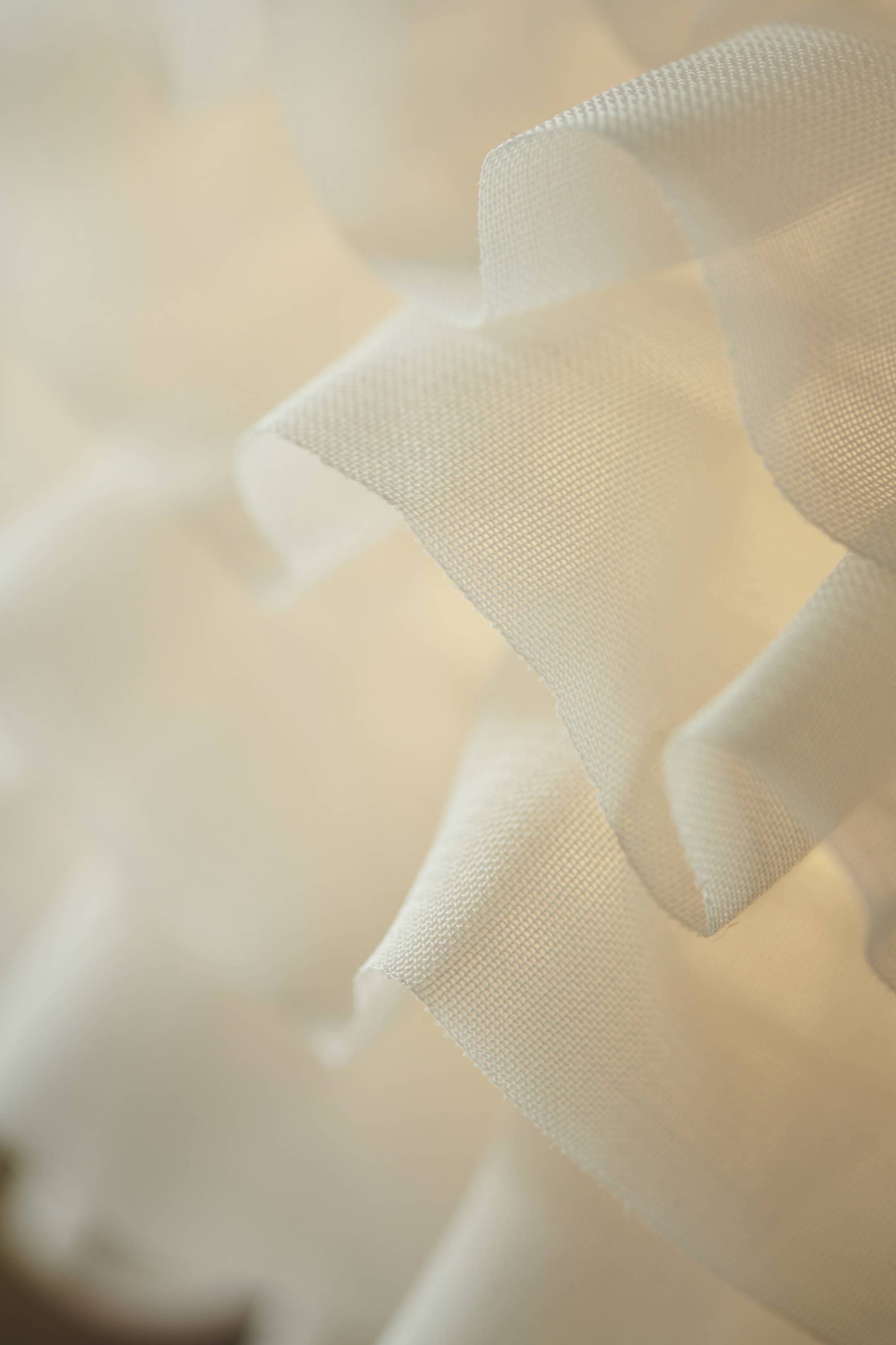 Nahaufnahme eines weißen, gewellten Stoffes mit weicher Beleuchtung im Hintergrund, die eine sanfte und elegante Textur vermittelt.