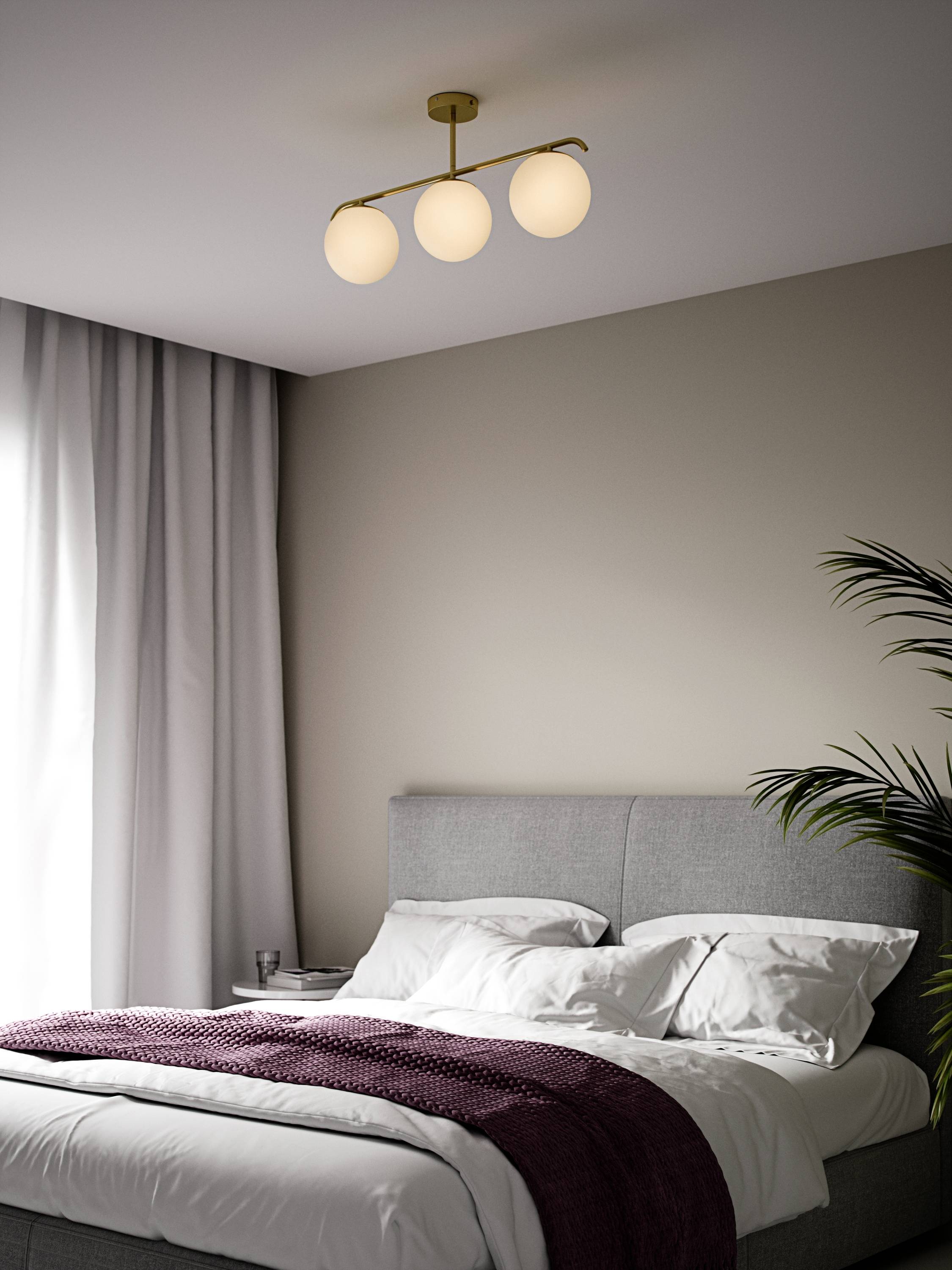 Ein graues Bett mit weißen Kissen und Decken, dazu eine lilafarbene Decke. Eine dreigliedrige Lampe hängt an der Decke.