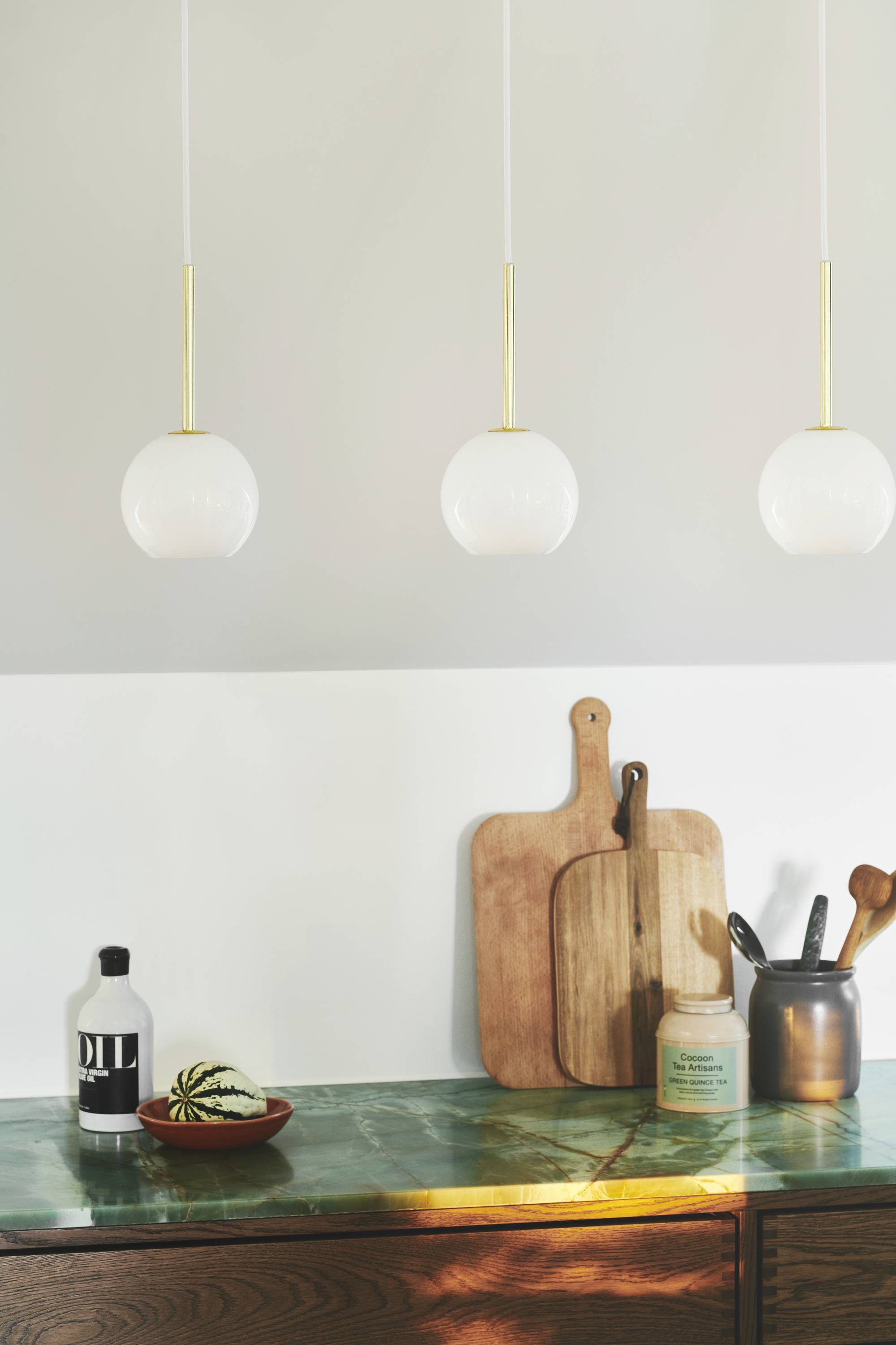 Drei hängende Lampen über einer Küchenzeile mit grüner Marmorplatte, Schneidebrettern und Küchenutensilien in einem stilvollen, modernen Raum.