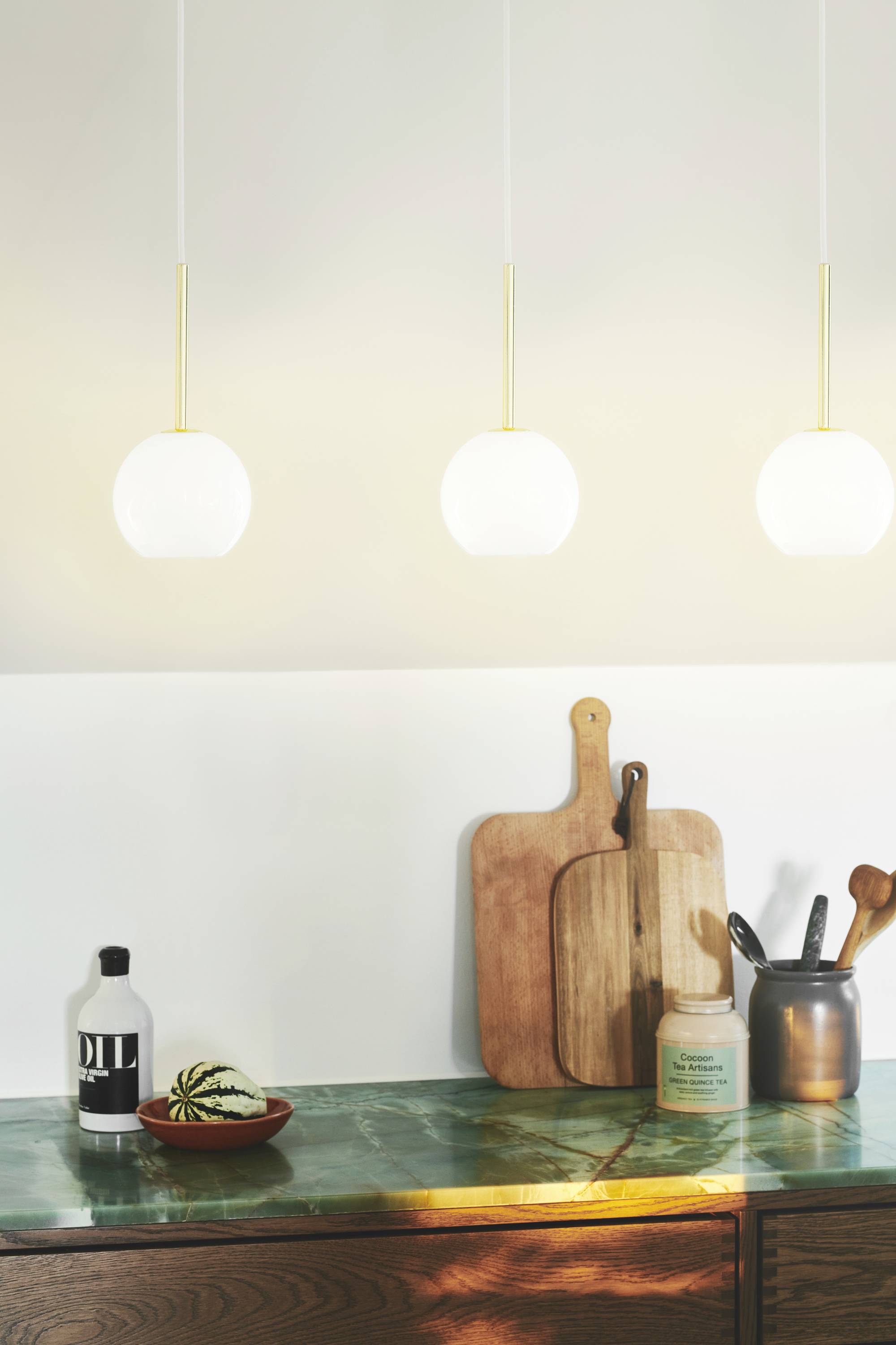 Drei hängende Lampen über einer Marmorküchenzeile mit Schneidebrettern, einer Dose, einer Flasche und einer kleinen Kürbisdeko.