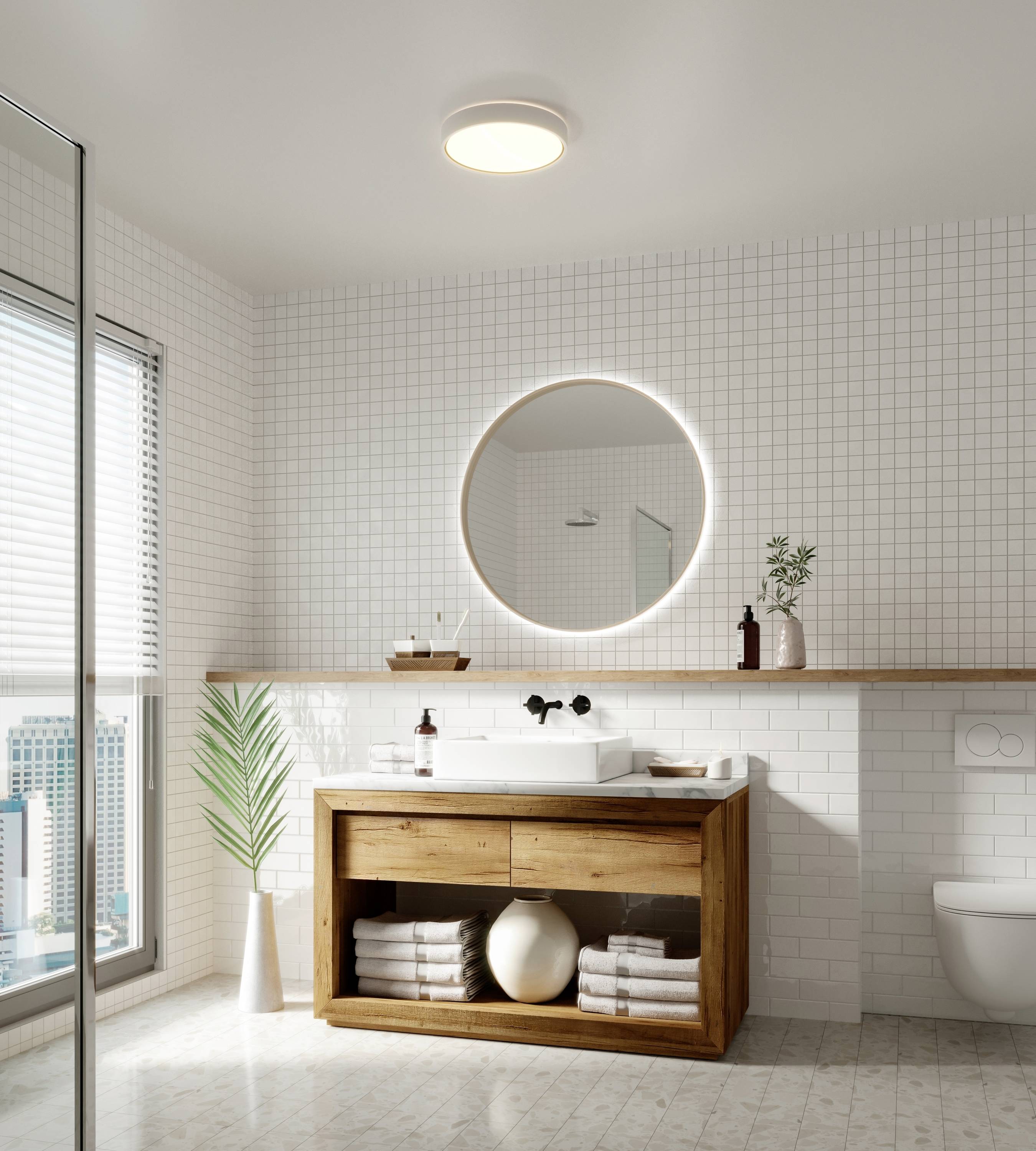 Helles Badezimmer mit Holzkommode, rundem Spiegel und Pflanzen. Fenster rechts mit Stadtblick. Minimalistisches Design.