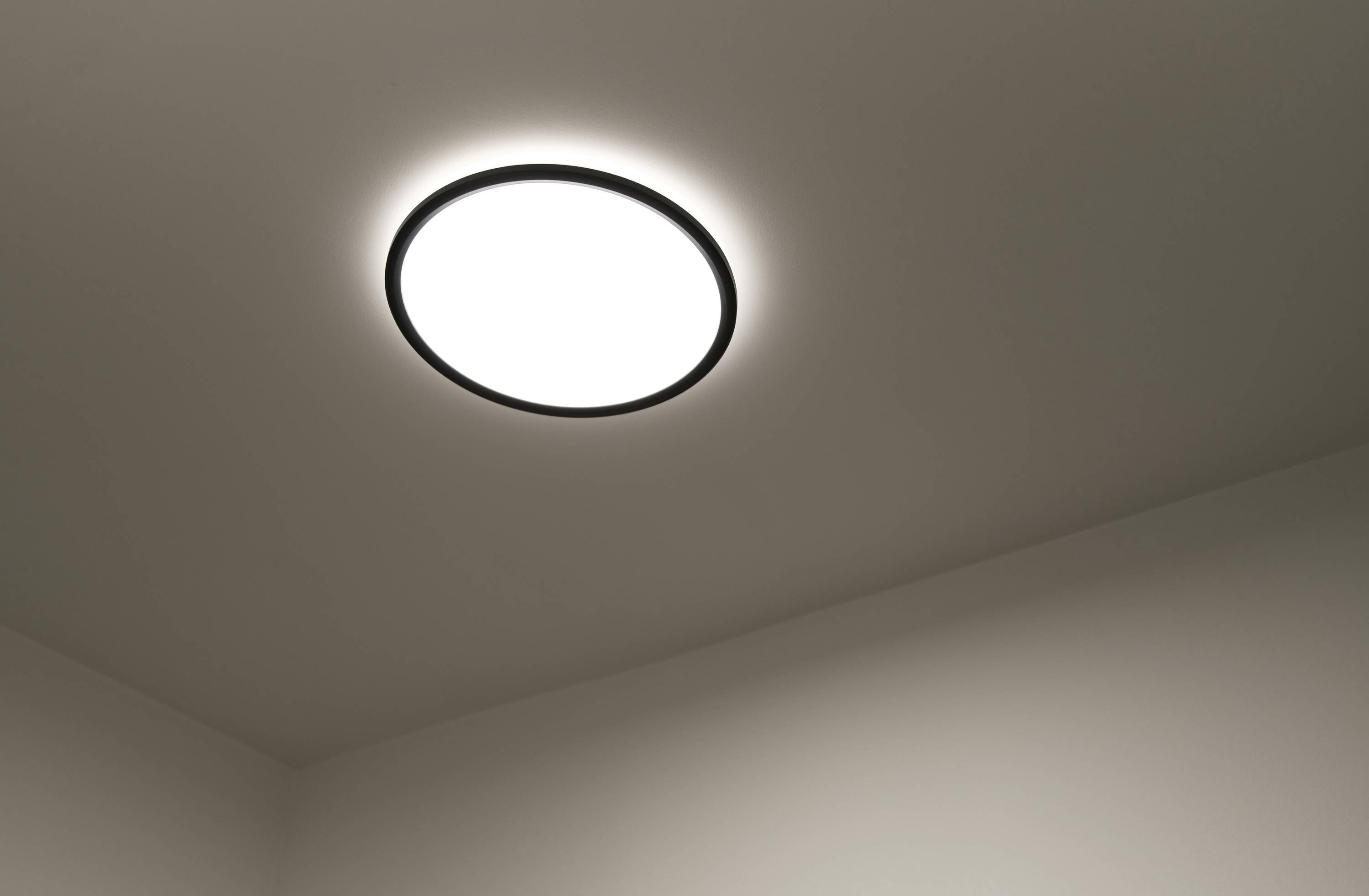 Leuchtende Deckenlampe in einem Raum. Diffuses Licht verbreitet sich gleichmäßig über die Decke. Keine weiteren Details sichtbar.