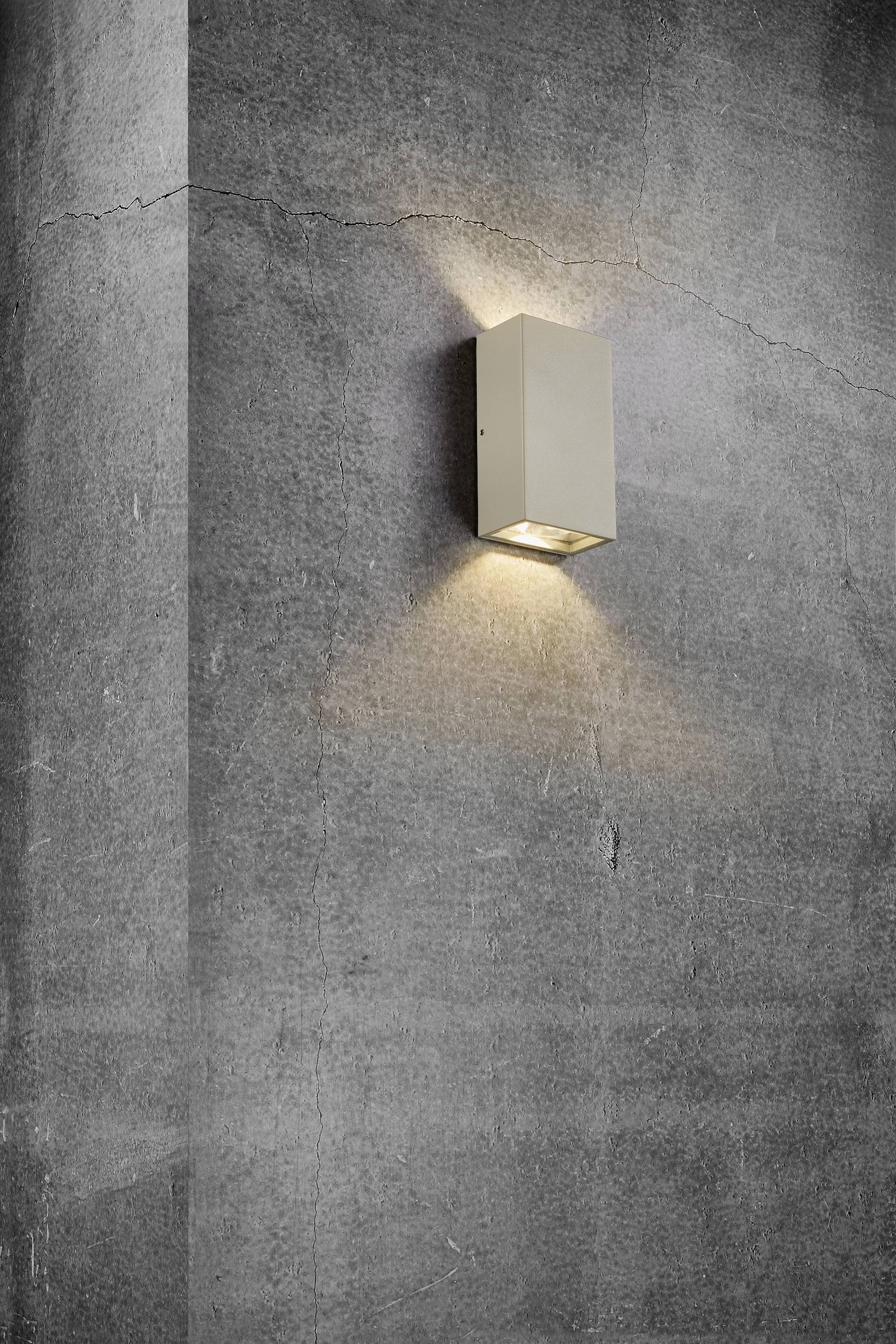 Wandleuchte an einer Betonwand, strahlt Licht nach oben und unten aus, erzeugt dadurch dezente Lichtakzente.