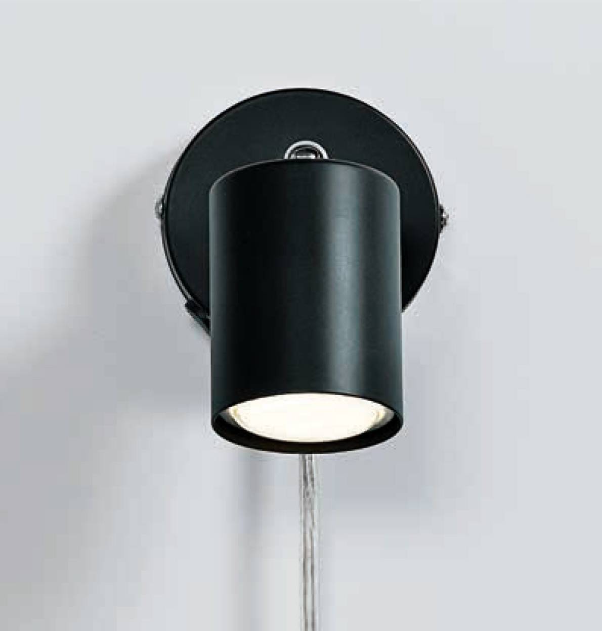 Wandlampe aus schwarzem Metall, zylindrische Form mit nach unten gerichtetem Licht, an einer grauen Wand montiert.