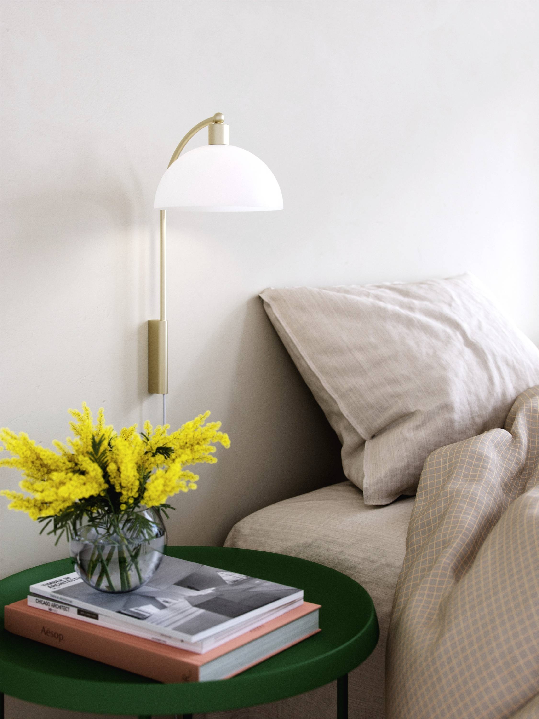 Ein gemütliches Schlafzimmer mit einem Bett, daneben ein grüner Tisch mit gelben Blumen in einer Vase und Büchern.