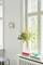 Vase mit bunten Blumen auf Fensterbank, daneben Bücher und eine grüne Glasschale. Helle, luftige Raumgestaltung mit großen Fenstern.