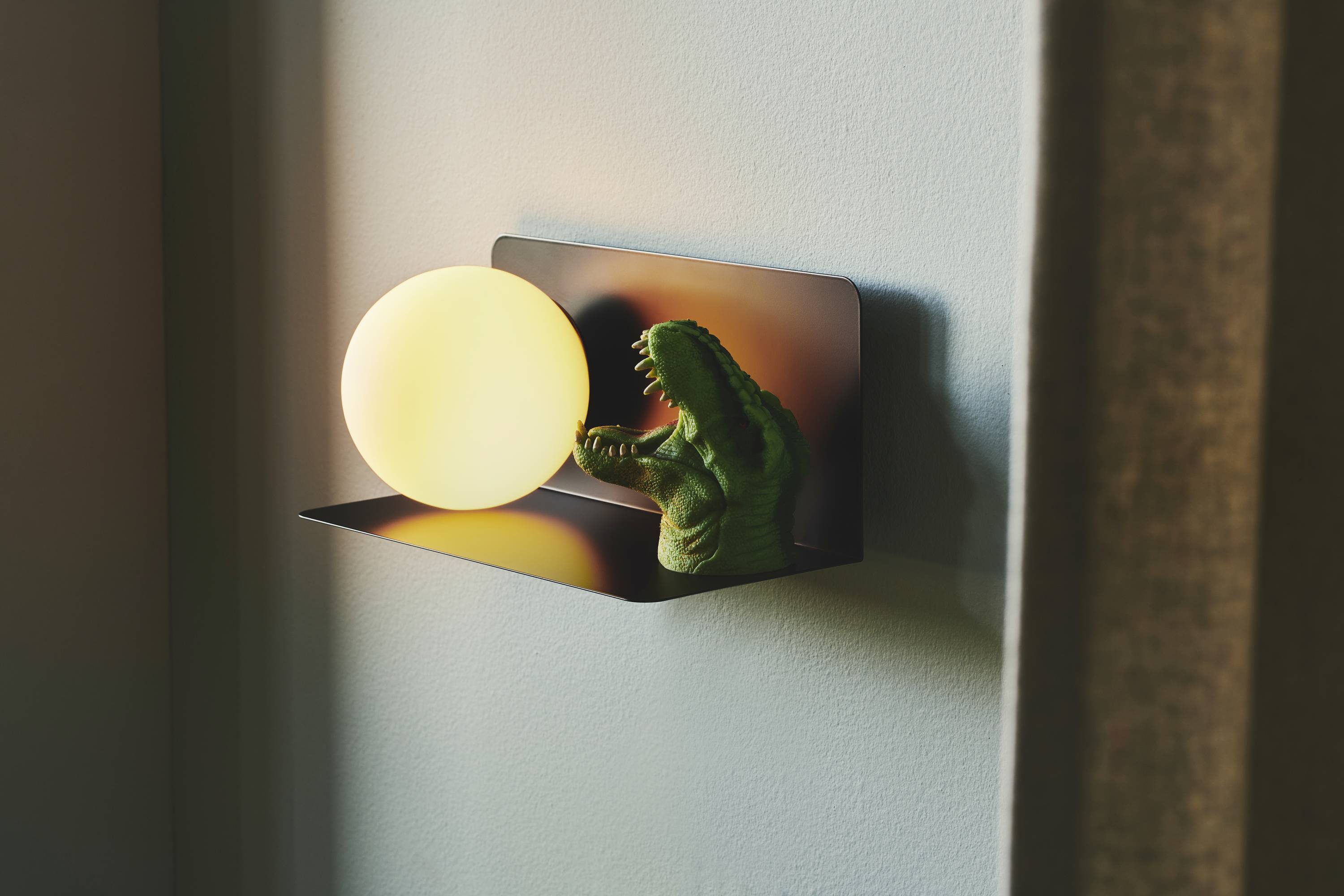 Ein Krokodilspielzeug auf einem Regal greift nach einem runden, leuchtenden Nachtlicht an der Wand.