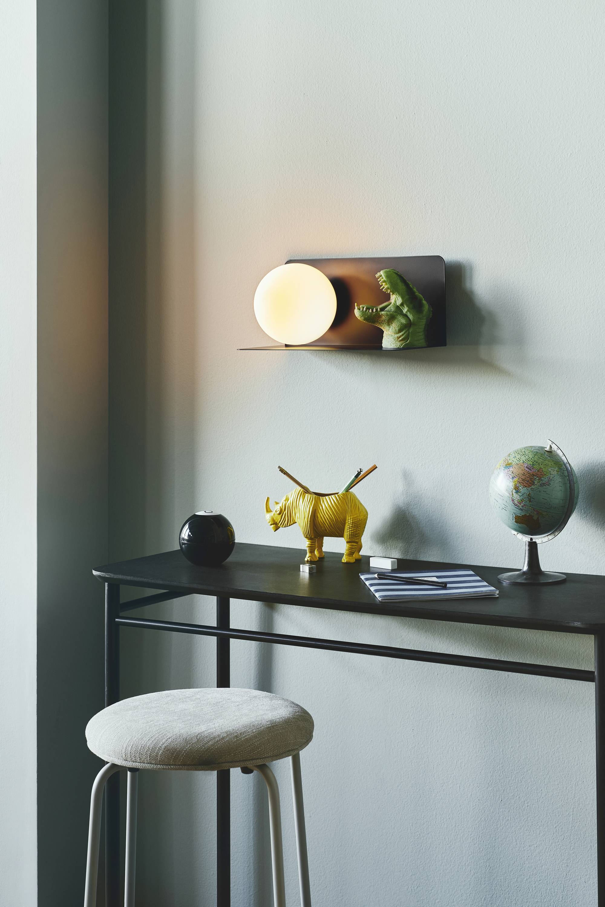 Ein moderner Schreibtisch mit einem Hocker, dekoriert mit einem gelben Rhinozeros, einem Globus und einer Wandlampe.