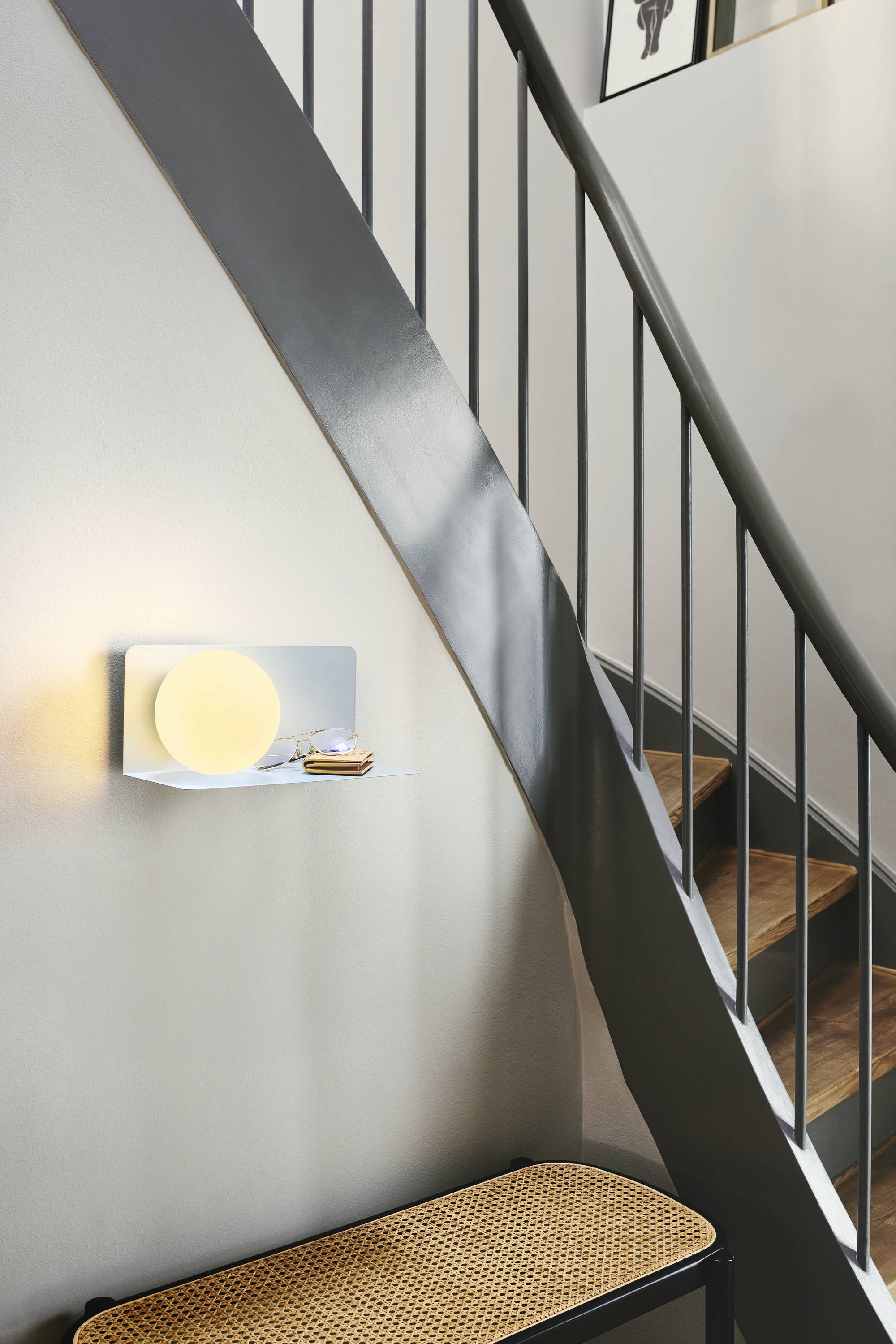 Eine moderne Treppe aus Holz und Metall. An der Wand eine kleine Ablage mit einer Lampe und zwei aufliegenden Büchern.