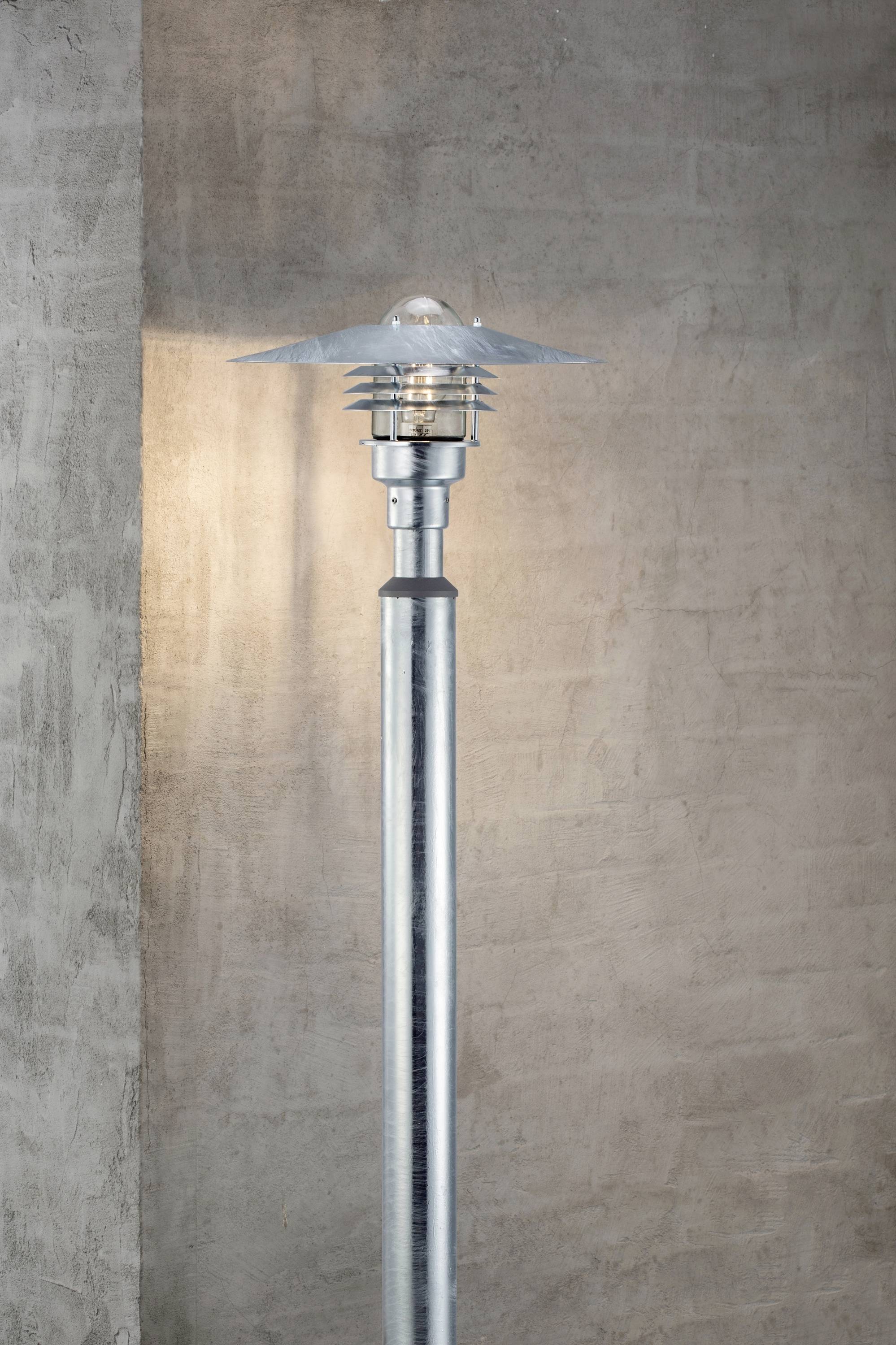 Laterne aus Metall mit modernem Design an einer Betonwand montiert, beleuchtet das Umfeld in einem warmen Licht.