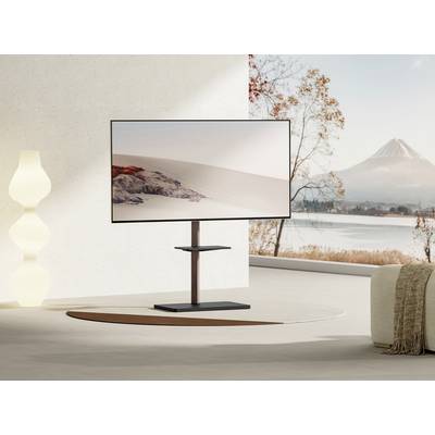 Moderner Fernseher auf einem Ständer in einem stilvollen Wohnzimmer mit großem Fenster, das eine Landschaft mit Bergen und einem See zeigt.