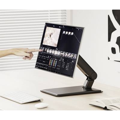 Eine Hand zeigt auf einen Monitor mit einer Videobearbeitungssoftware auf einem Schreibtisch. Im Hintergrund sind Jalousien zu sehen.