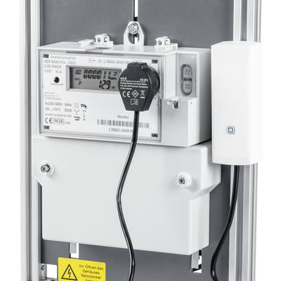 Ein digitaler Stromzähler zeigt den aktuellen Verbrauch an. Ein schwarzes Kabel ist angeschlossen. Ein Warnschild unten weist auf Vorsicht hin.