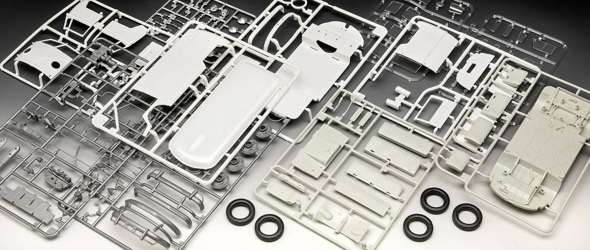 'Plastikmodellbausatz eines Fahrzeugs, bestehend aus grauen und weißen Rahmen mit Einzelteilen sowie kleinen Gummireifen.'
