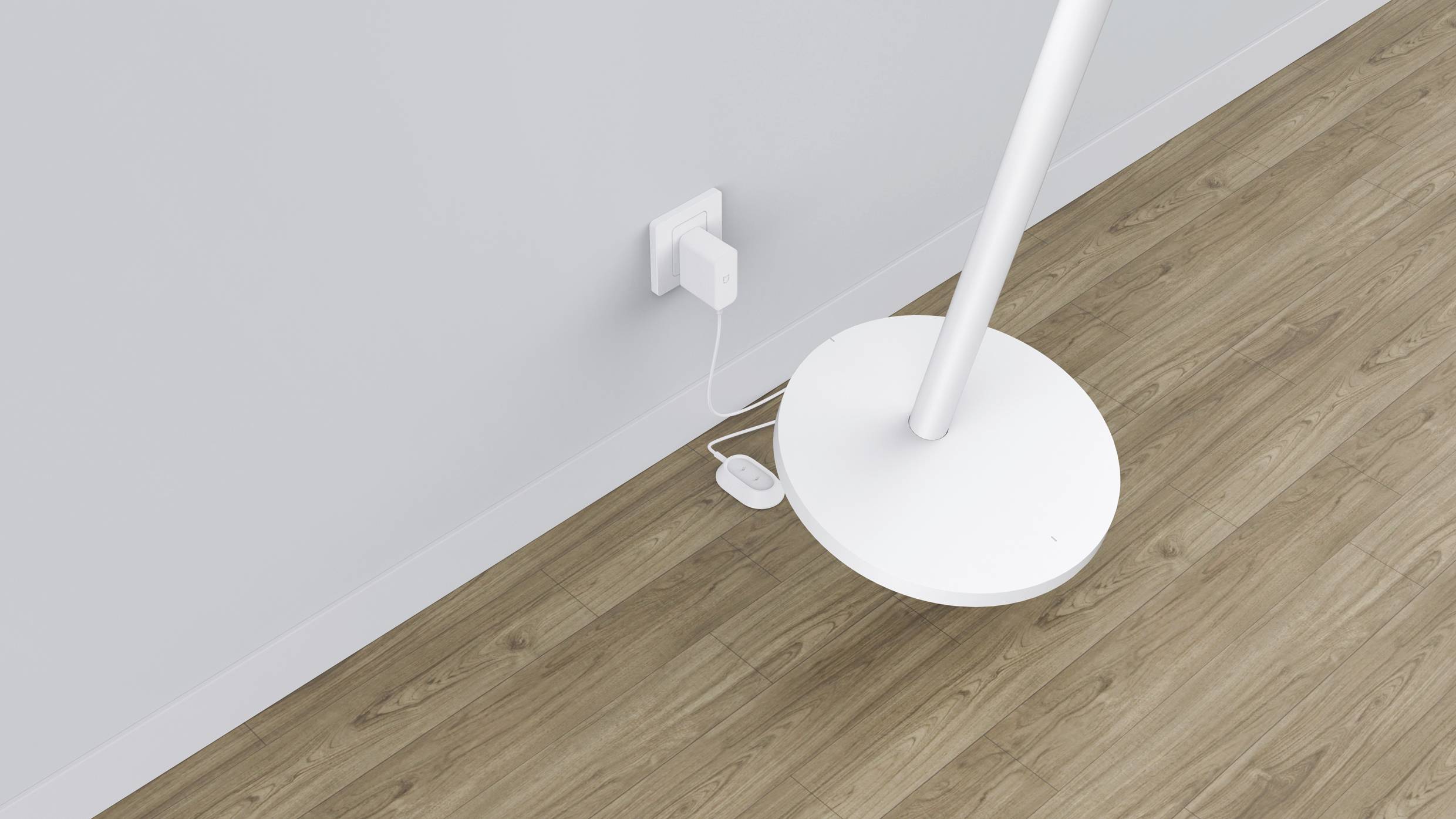 Stehlampe mit rundem Fuß steht auf Holzboden. Behälter an der Wand liefert Strom zum angeschlossenen Kabel.