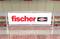 Ein Werbeschild in einer U-Bahn-Station zeigt das Logo der Marke 'fischer' mit einem roten Schriftzug und Symbol.