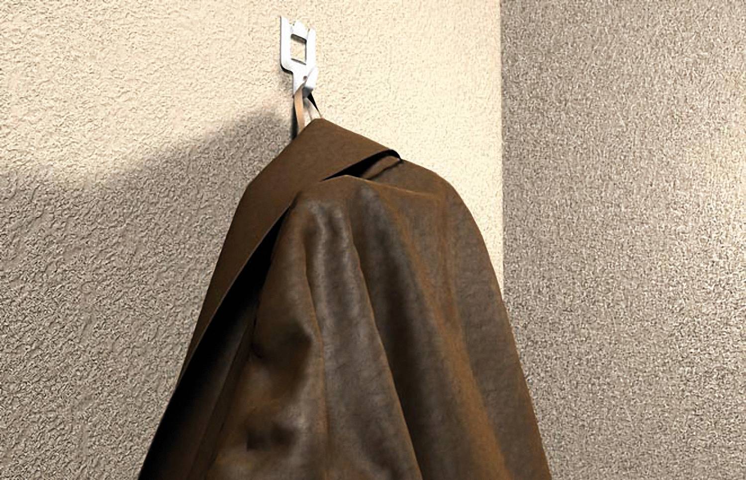 Brauner Mantel, der an einem Wandhaken an einer strukturierten beigen Wand hängt.