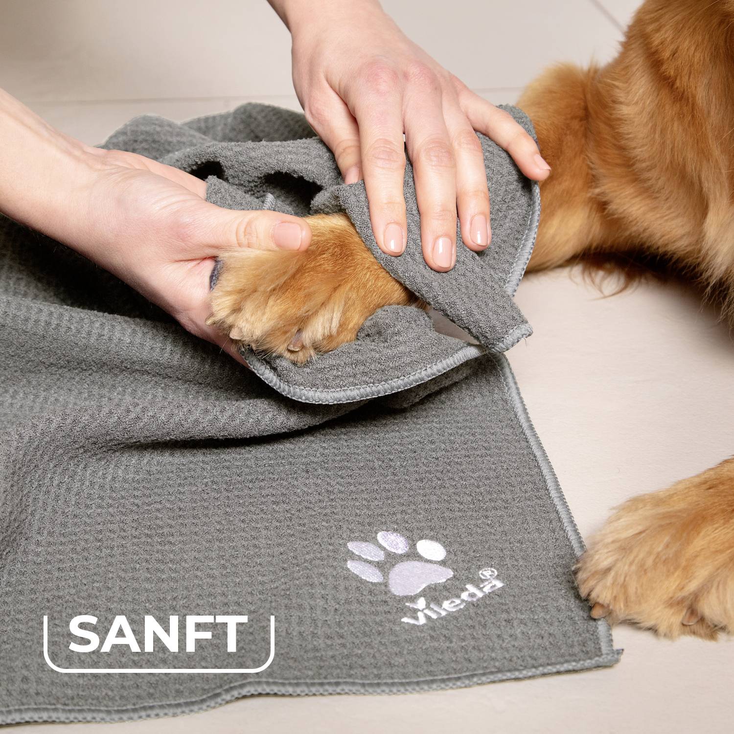 Ein Hund wird sanft mit einem grauen Handtuch abgetrocknet. Links unten steht das Wort 'SANFT' neben einem Pfotenabdruck.