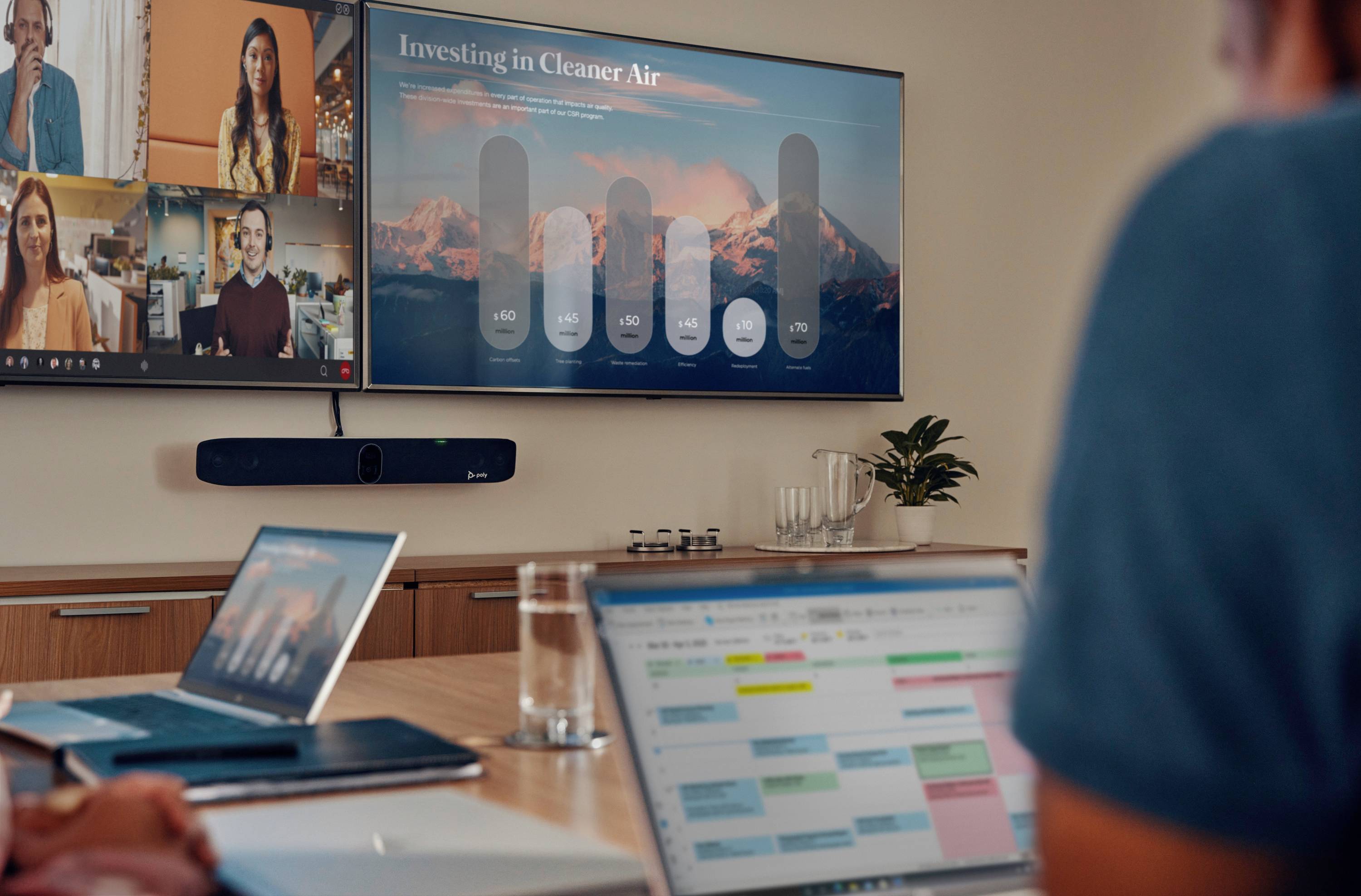 Personen in einem Videokonferenzraum. Ein Bildschirm zeigt eine Präsentation mit dem Titel 'Investing in Cleaner Air' und Daten.