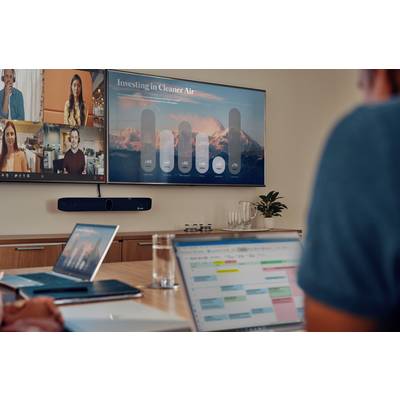 Personen in einem Videokonferenzraum. Ein Bildschirm zeigt eine Präsentation mit dem Titel 'Investing in Cleaner Air' und Daten.