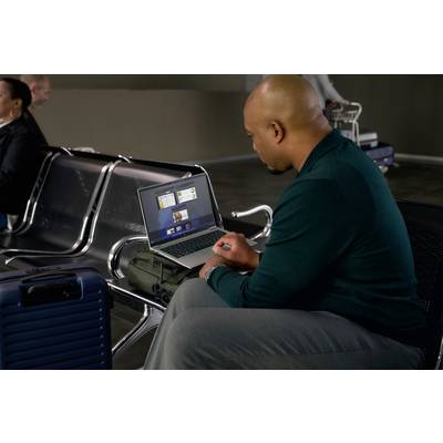 Ein Mann sitzt in einem Wartebereich am Flughafen und arbeitet auf einem Laptop, der auf seinem Handgepäck platziert ist.