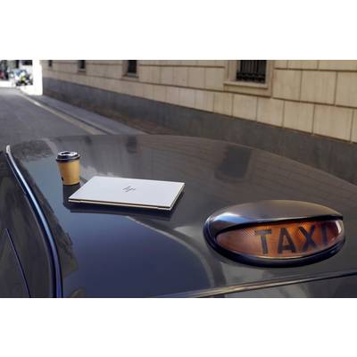 Ein Laptop und ein Kaffeebecher stehen auf dem Dach eines Taxis. Im Hintergrund sieht man eine Straße mit Gebäuden.