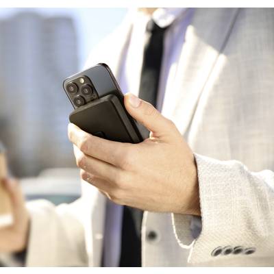 Ein Mann in einem hellen Anzug hält ein Smartphone und einen Kaffeebecher. Im Hintergrund sind unscharfe Gebäude zu sehen.