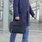 Eine Person in blauer Jacke und Jeans trägt eine dunkelblaue Aktentasche und steht vor einem modernen Glasgebäude.