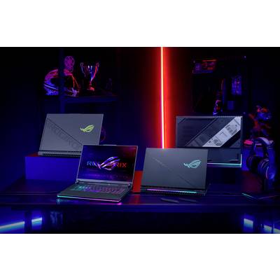 Drei Laptops auf einem Tisch in einem beleuchteten Raum. Im Hintergrund sind ein Helm, ein Pokal und Computerzubehör zu sehen.
