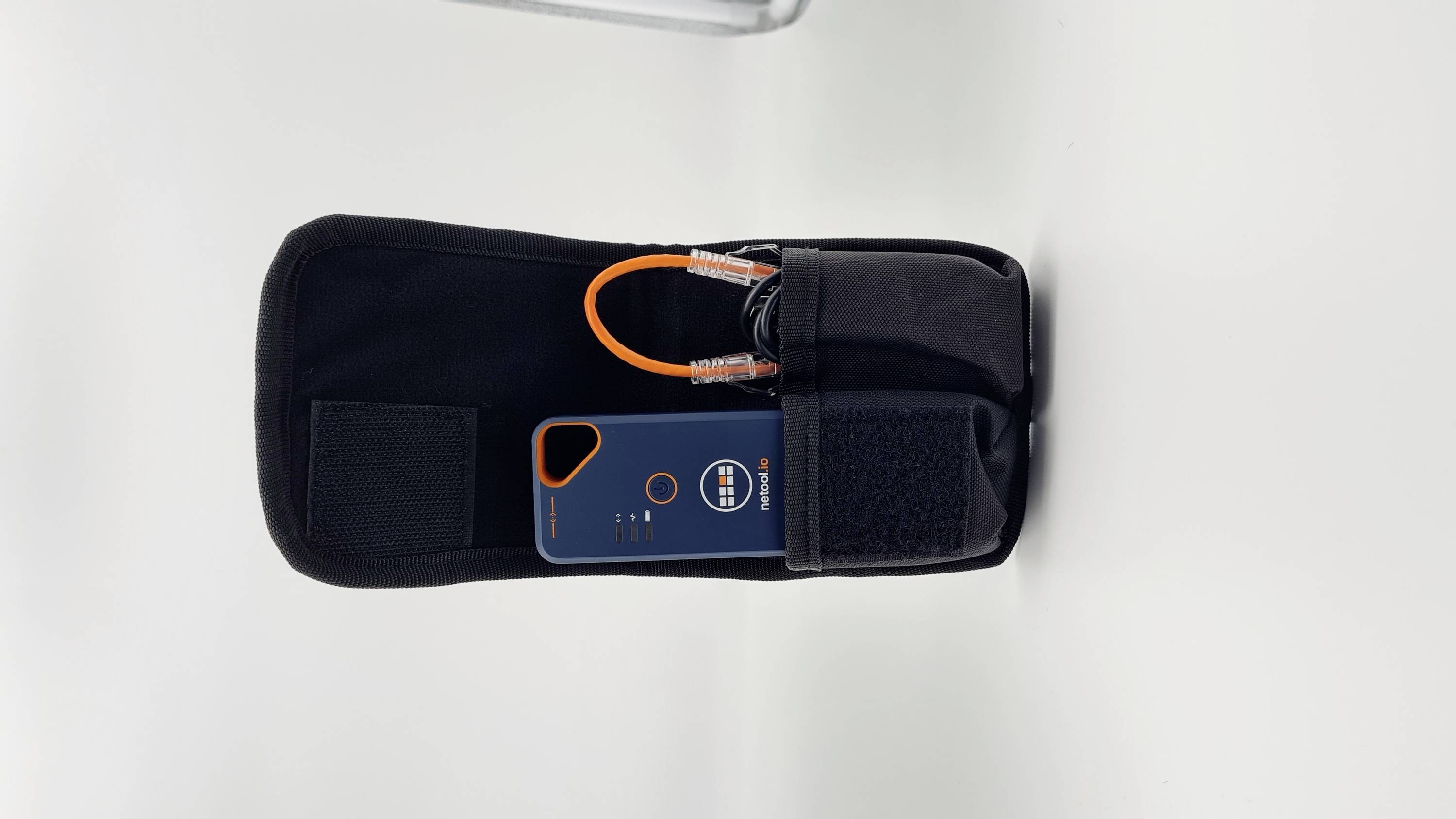 Ein schwarzes Etui mit Klettverschluss enthält ein blaues Gerät mit Digitalanzeige und verkabeltem Stecker, auf weißem Hintergrund.