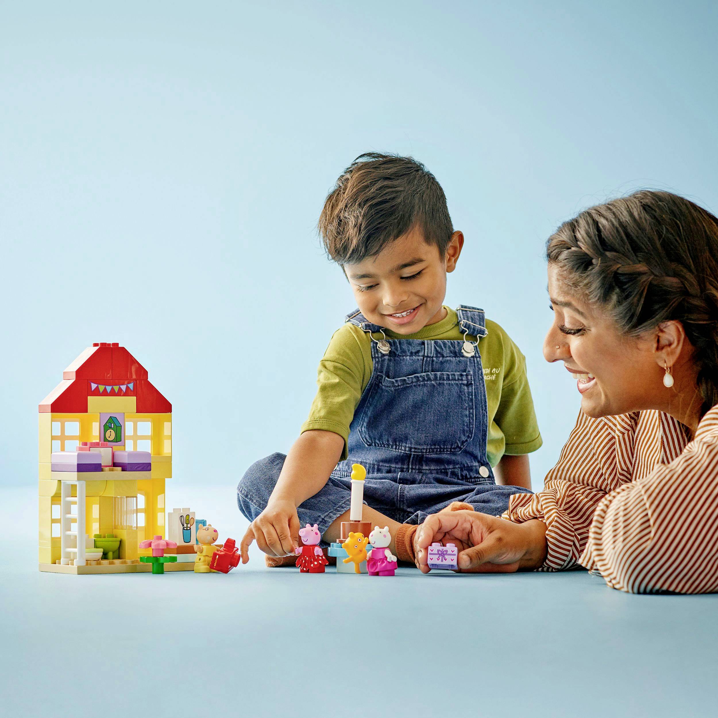 Ein Junge und eine Frau spielen mit bunten Bauklötzen und einem Puppenhaus vor einem blauen Hintergrund.