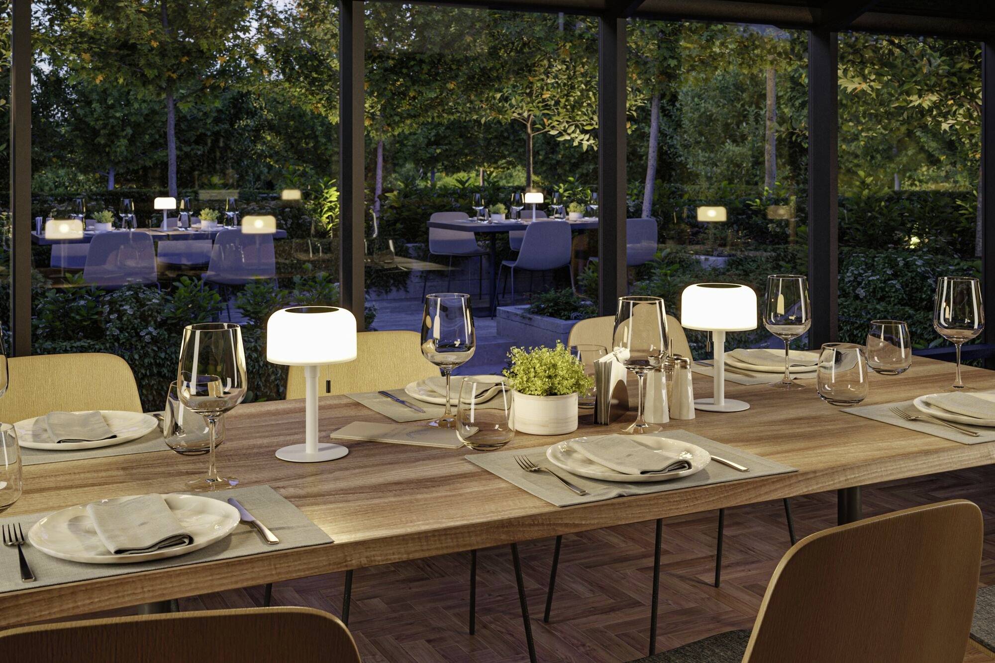 Ein elegant gedeckter Tisch in einem Restaurant mit Waldsicht im Hintergrund. Teller, Gläser und schlichte Tischlampen sind arrangiert.