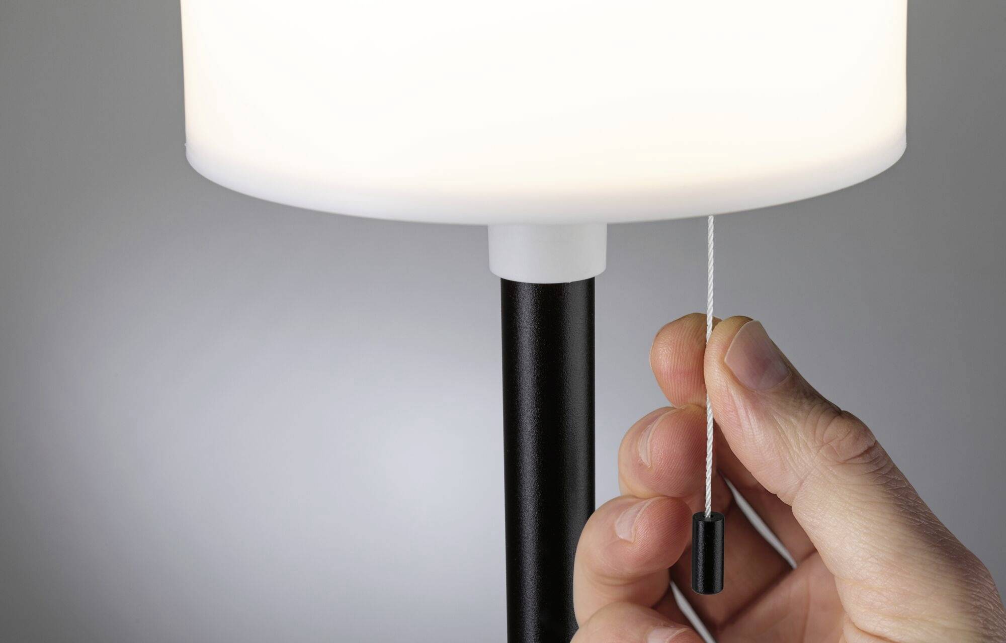Person zieht an der Schnur einer eingeschalteten weißen Stehlampe.