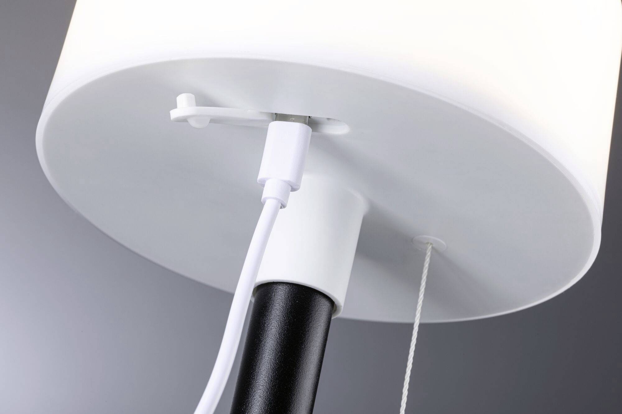 Ansicht einer Tischlampe von unten, die das Kabel und den Zugschalter zeigt. Der Lampenschirm ist weiß und beleuchtet.