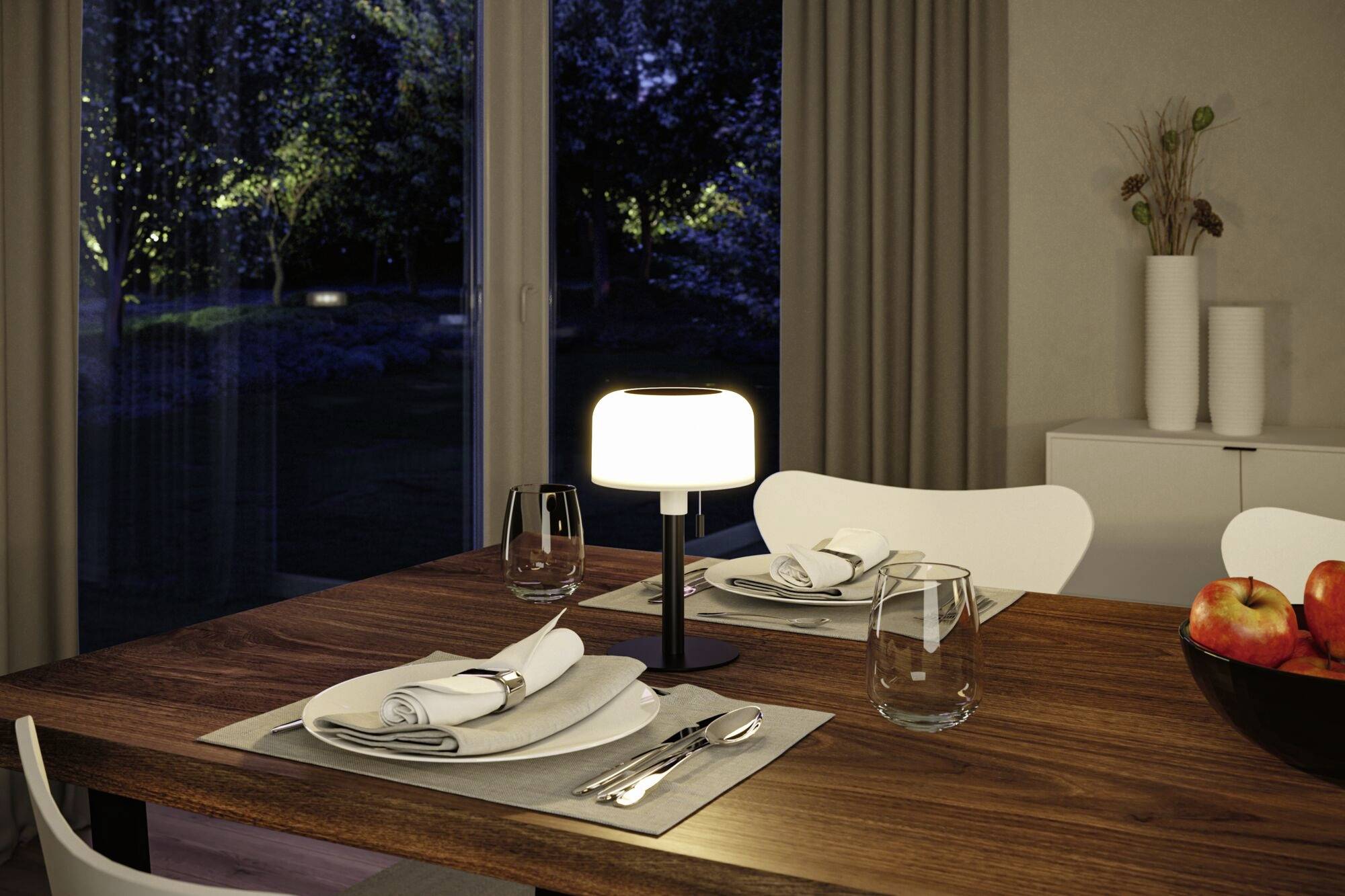 Ein gedeckter Esstisch mit Geschirr und Besteck, dekoriert mit einem leuchtenden Tischlampe in einem modernen Esszimmer bei Nacht.