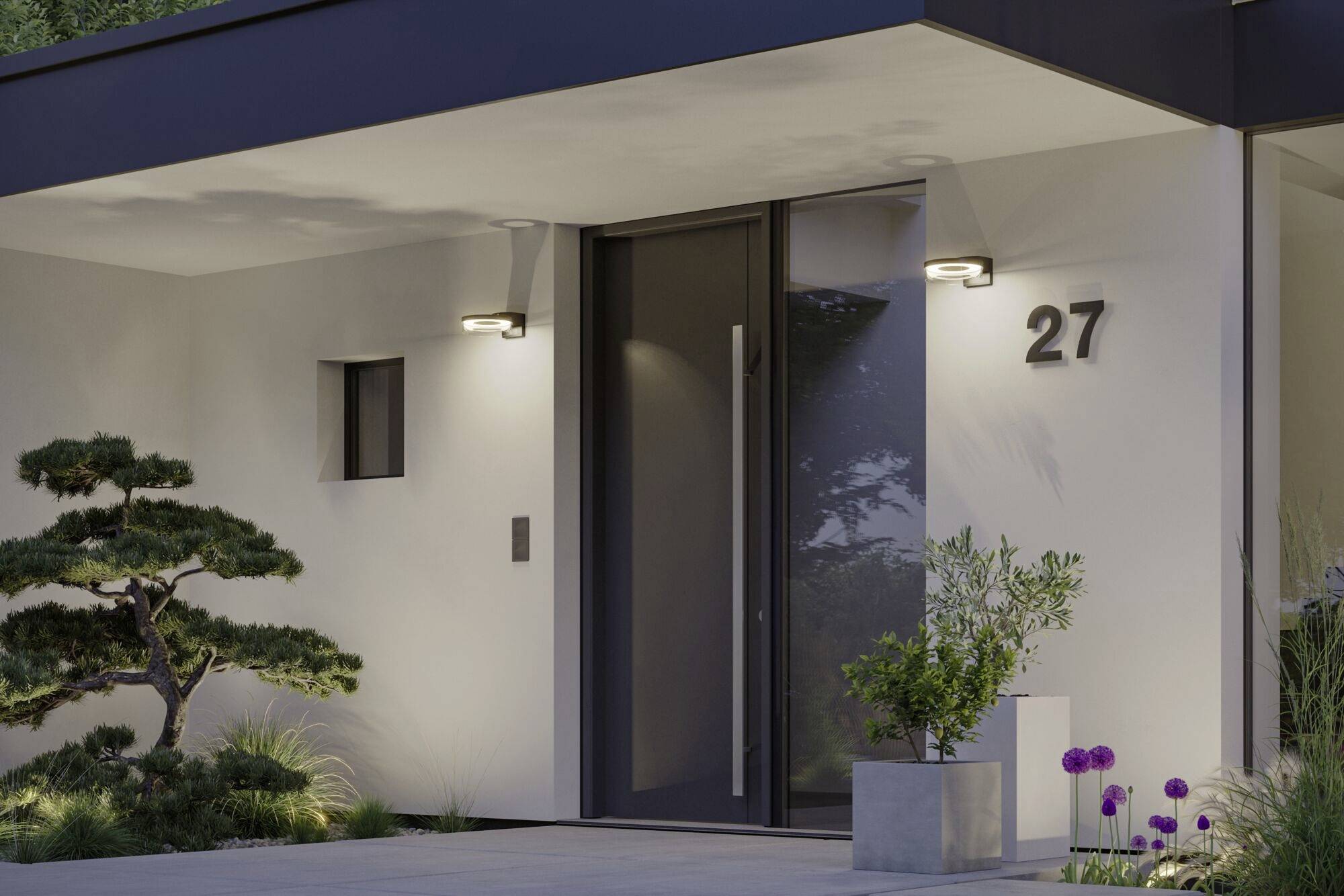 Ein modernes Haus mit einer schwarzen Tür, außen zwei Wandleuchten und der Hausnummer '27'. Links ein kleiner Baum und ein Betonpflanzkübel.