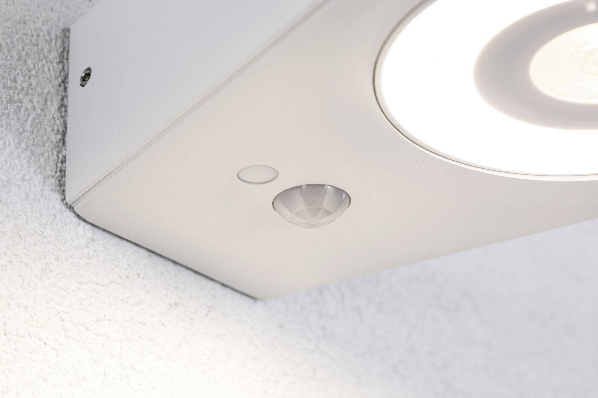 Eine Deckenleuchte mit eingebautem Bewegungsmelder, montiert an einer weißen Wand. Die Lampe ist eingeschaltet.