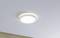 Runde, weiße Deckenleuchte mit einfachem, modernem Design, die an einer glatten, hellgrauen Decke montiert ist. Es leuchtet gleichmäßig.