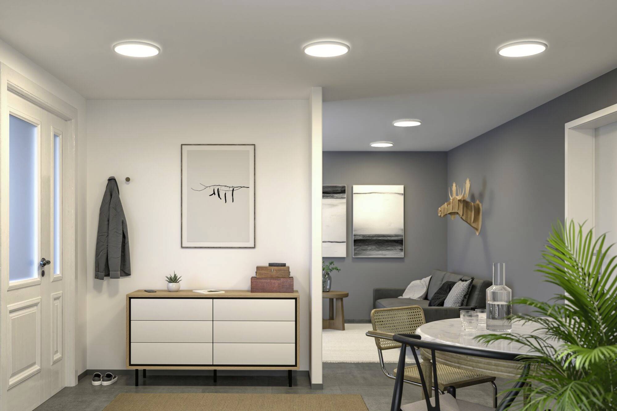 Wohnzimmer mit modernem Design. Links ein Sideboard mit Kunstbild darüber, rechts ein Esstisch und Sofa im Hintergrund, Pflanzen und Haken an der Wand.