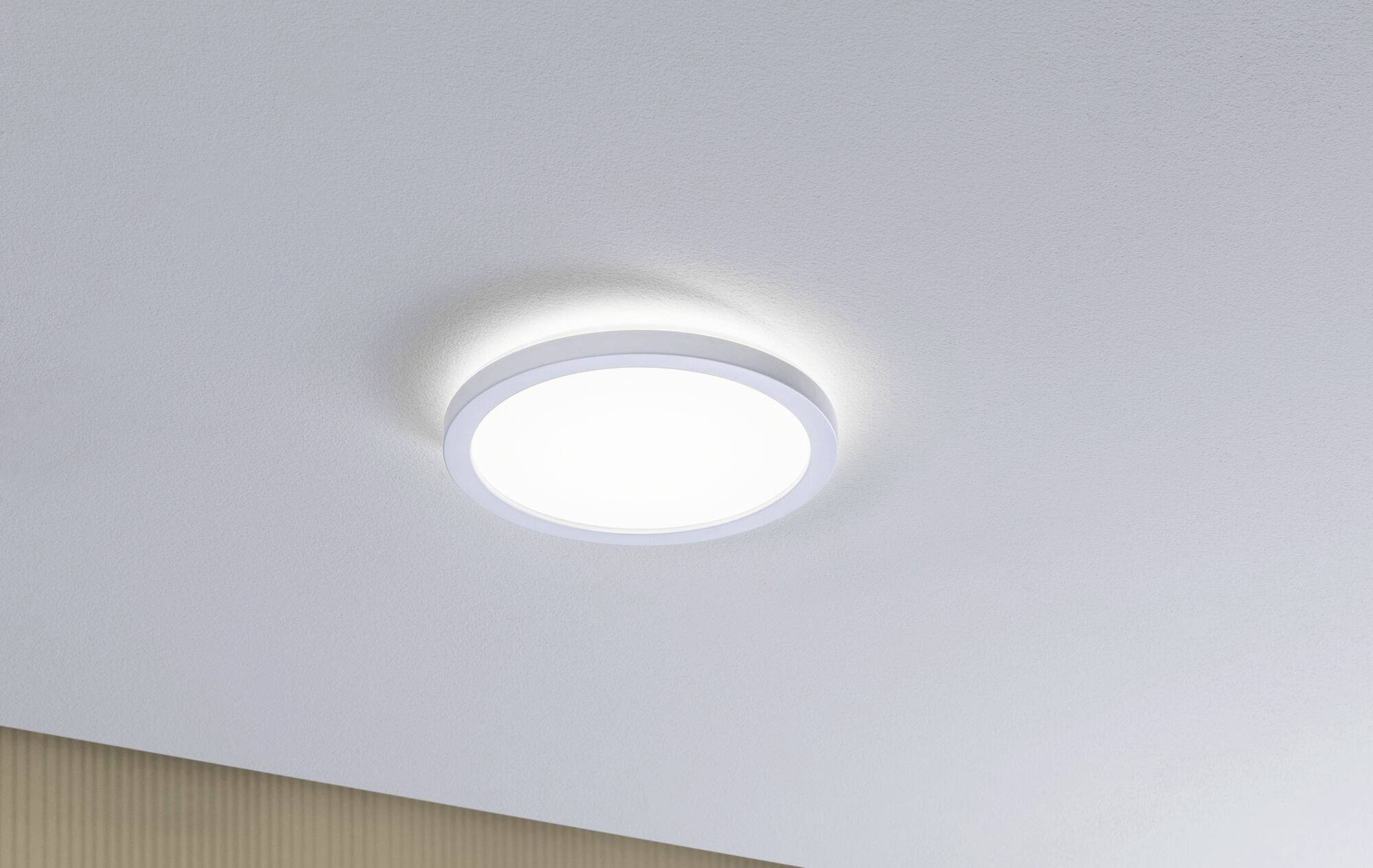 Runde, weiße Deckenlampe leuchtet an einer hellen Decke. Umgebung ist minimalistisch.