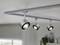 Deckenstrahler mit drei ausrichtbaren Lampen in modernem Design, montiert an einer Schiene in einem hellen Raum mit Pflanzen im Hintergrund.