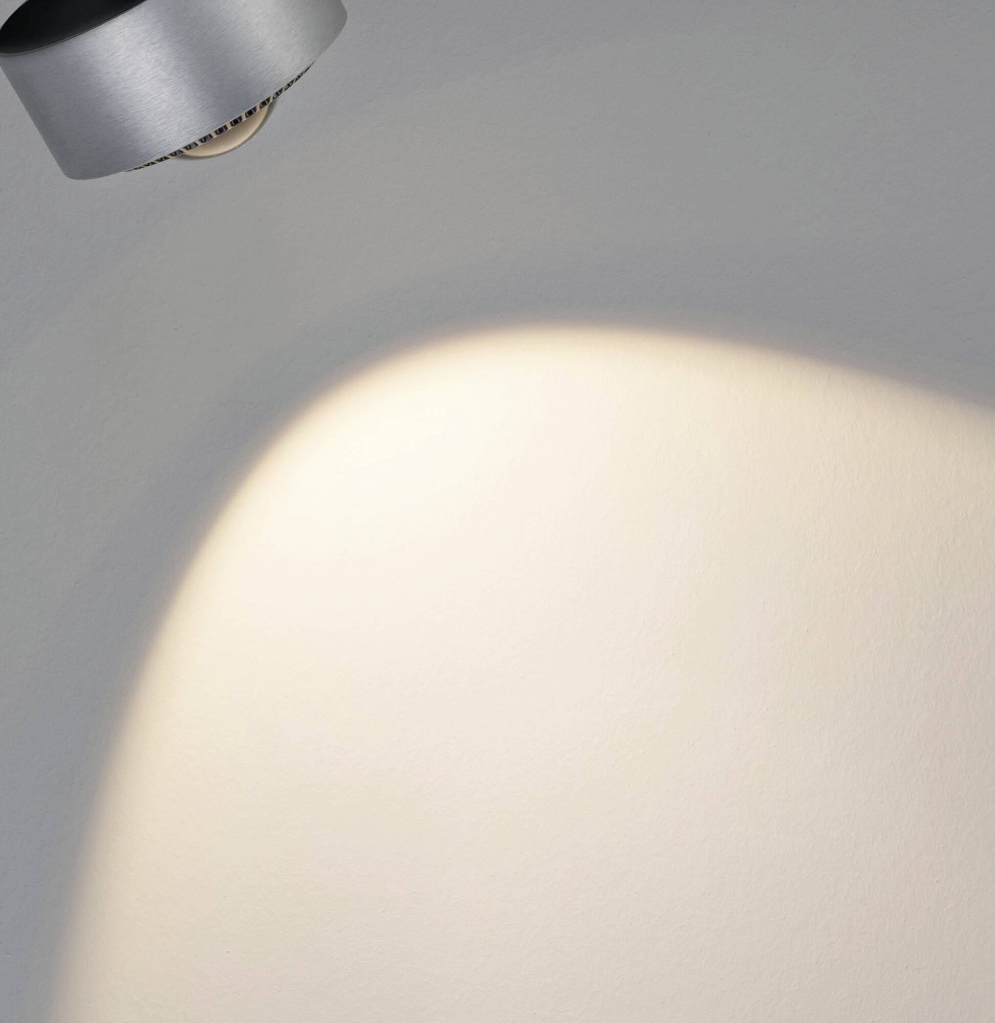 Ein Scheinwerfer an der Decke beleuchtet einen weißen Wandbereich, erzeugt eine ovale Lichtfläche.