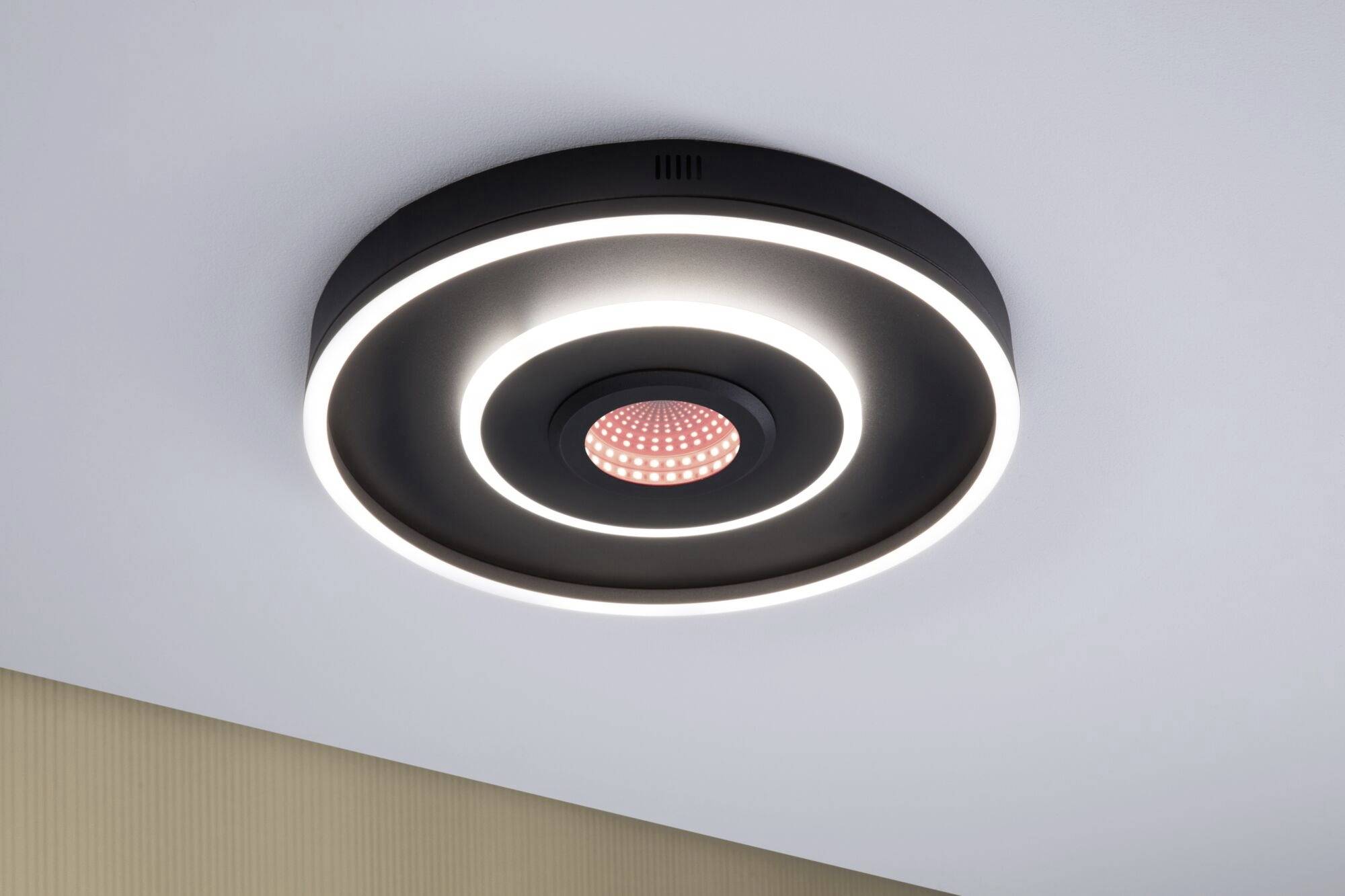 Runde Deckenlampe mit schwarzem Gehäuse und mehreren leuchtenden LED-Ringen, im Zentrum ein roter Punkt. Moderner, minimalistischer Stil.